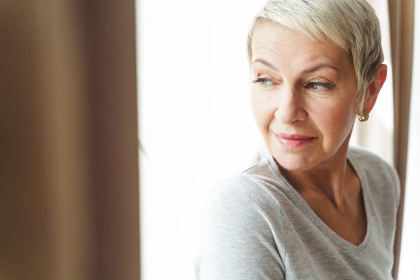 istock Calm aged woman standing by the window 1213917956
