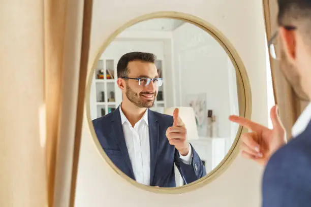 Waist-up portrait of a handsome stylish young Caucasian man looking at himself in the mirror