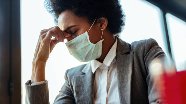 Black businesswoman with protective face mask holding her head in pain. Exhausted African American businesswoman with face mask having a headache while sitting in a cafe. avian flu virus photos stock pictures, royalty-free photos & images