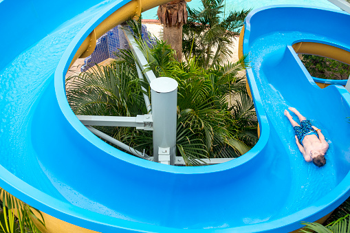 This picture shows a top view perspective of a boy sliding down a blue waterslide.