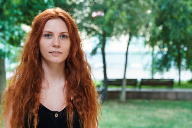 Pretty young smiling teenager girl with red curly shiny hair is wearing green sweater in autumn park.