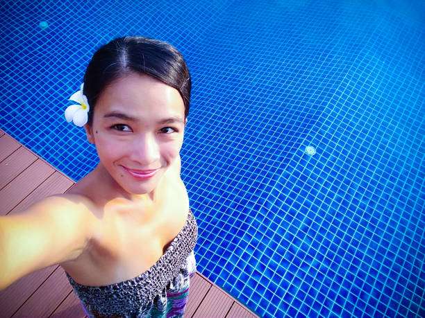 A young Asian Thai woman taking a selfie photo at the swimming pool on holiday vacation freedom lifestyle in summer.