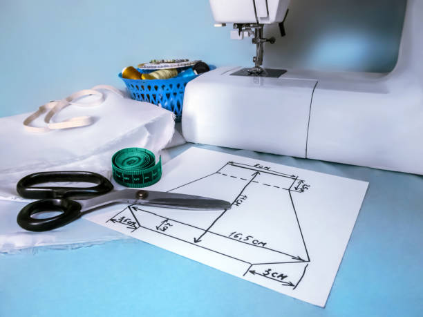 Handmade sewing pattern of a face mask lies near the sewing machine and sewing accessories stock photo