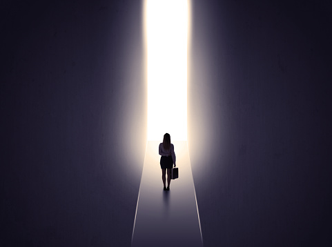 Young businesswoman stands in dark tunnel and looks in the glowing end