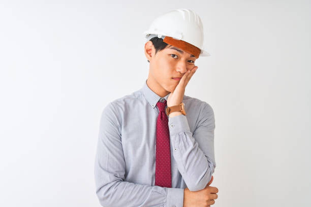 Chinese architect man wearing tie and helmet standing over isolated white background thinking looking tired and bored with depression problems with crossed arms. Chinese architect man wearing tie and helmet standing over isolated white background thinking looking tired and bored with depression problems with crossed arms. lazy construction laborer stock pictures, royalty-free photos & images