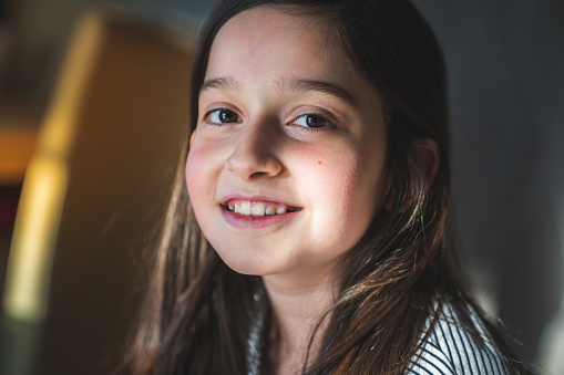 One small caucasian girl ten years old with curly hair front view portrait close up standing in front of white background looking to the camera pointing finger to copy space smiling happy and joy