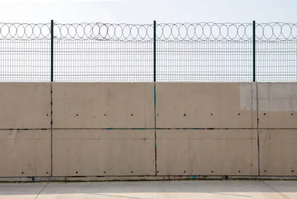 Photo of Razor wire with its sharp steel barbs on top of a concrete wall