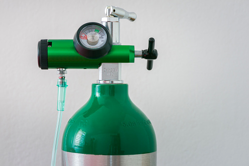 Close up of an oxygen regulator gauge and cylinder with white background