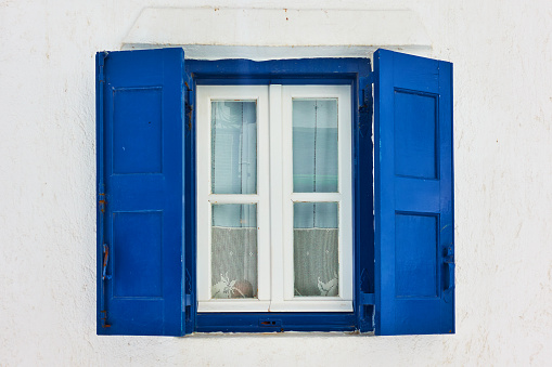 Window of greek whitewashed house with trditional blue shutters in Mykonos island, Greece
