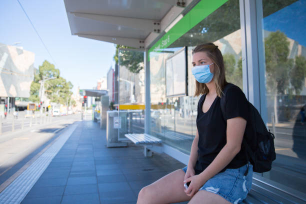 jovem mulher usando uma máscara facial sentada sozinha em uma parada de bonde - melbourne tourist people traveling women - fotografias e filmes do acervo