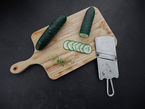 Fresh sliced cucumber with mandoline on a wooden board