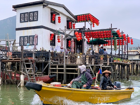 Tai O, Hong Kong - January 18, 2020: The fishing boat with stilt houses of Tai O in the background. Tai O is a fishing town located on the western side of Lantau Island in Hong Kong. It is home to the Tanka people, a community of fisher folk who’ve built their houses on stilts above the tidal flats of Lantau Island for generations.