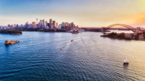 Sydney harbour at sunset around major city landmarks from Fort Denison to the Sydney harbour bridge in elevated aerial view.