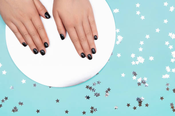 istock Womans hands with black manicure on silver circle and pastel blue background. 1213960836