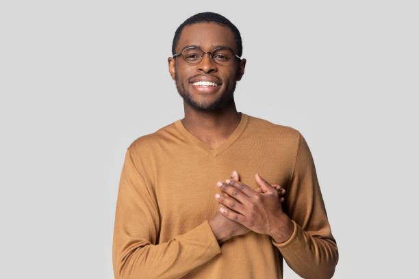 Head shot smiling African American man keeping hands on chest Head shot portrait close up smiling African American man in glasses keeping hands on chest, looking at camera, grateful young male feeling gratitude, appreciation, isolated on grey background in pride we trust stock pictures, royalty-free photos & images