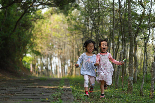 two smiling Asian twins girls running in a forest. background for happy family.