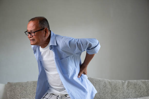 asian old man sitting on sofa and having a back pain, backache at home. senior healthcare concept. - lower back pain imagens e fotografias de stock
