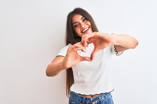 Young beautiful woman wearing casual t-shirt standing over isolated white background smiling in love showing heart symbol and shape with hands. Romantic concept.