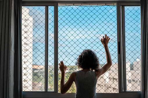 Bored girl looking through the window in quarantine during the world COVID-19 pandemic in 2020