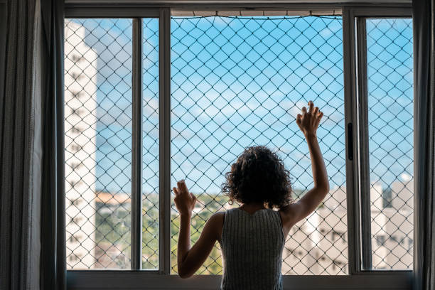 Boredom Bored girl looking through the window in quarantine during the world COVID-19 pandemic in 2020 window grid patterns stock pictures, royalty-free photos & images