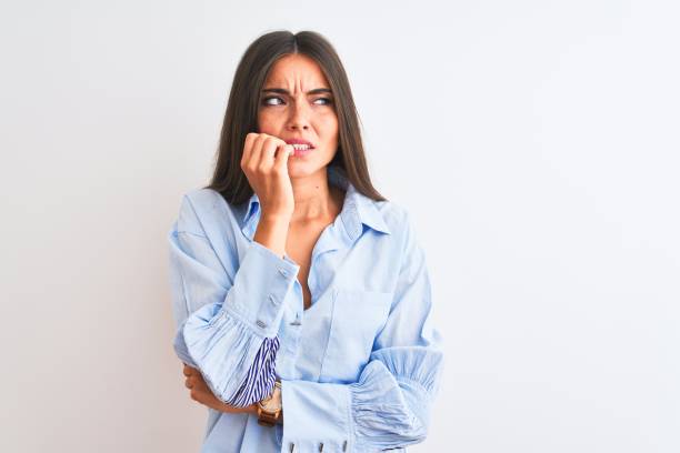 young beautiful woman wearing blue elegant shirt standing over isolated white background looking stressed and nervous with hands on mouth biting nails. anxiety problem. - nail biting imagens e fotografias de stock