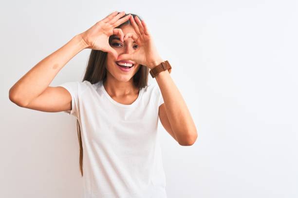 joven hermosa mujer con camiseta casual de pie sobre fondo blanco aislado haciendo forma de corazón con la mano y los dedos sonriendo mirando a través de signo - beautiful caucasian one person romance fotografías e imágenes de stock