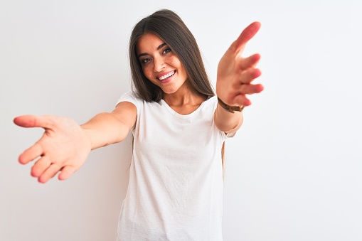 Young beautiful woman wearing casual t-shirt standing over isolated white background looking at the camera smiling with open arms for hug. Cheerful expression embracing happiness.