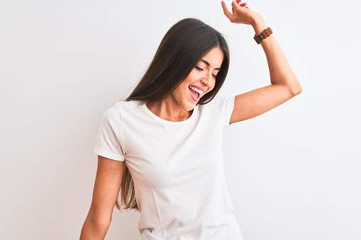 Young beautiful woman wearing casual t-shirt standing over isolated white background Dancing happy and cheerful, smiling moving casual and confident listening to music