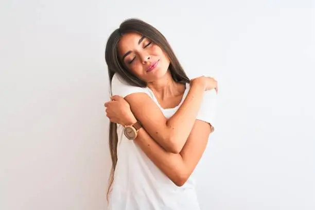 Young beautiful woman wearing casual t-shirt standing over isolated white background Hugging oneself happy and positive, smiling confident. Self love and self care