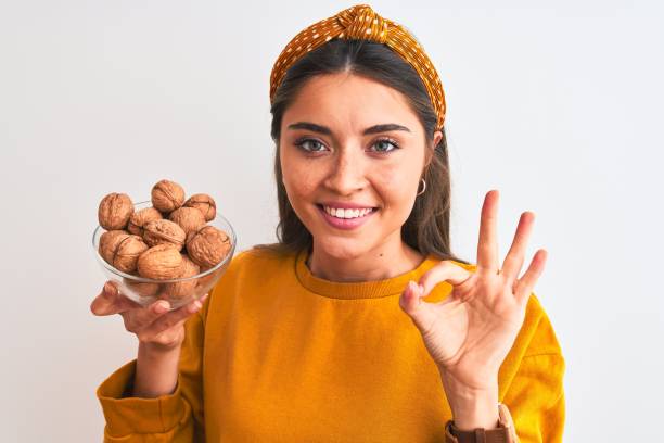 istock Young beautiful woman holding bowl with walnuts standing over isolated white background doing ok sign with fingers, excellent symbol 1213977651