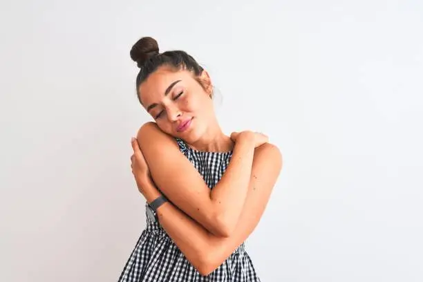 Beautiful woman with bun wearing casual dresss standing over isolated white background Hugging oneself happy and positive, smiling confident. Self love and self care