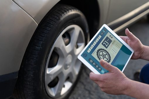 Close up of unrecognizable man checking the pressure on a punctured tire using a tablet - Technology concepts