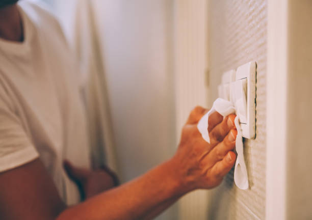 My light switch needs a good clean A man cleaning light switch with disinfectantat at home against virus. light switch photos stock pictures, royalty-free photos & images