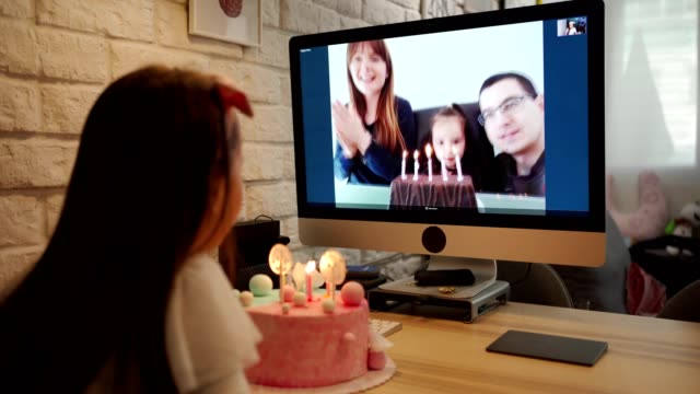 Birthday girl blowing birthday candles in home isolation while her family singing her Happy Birthday song via video app