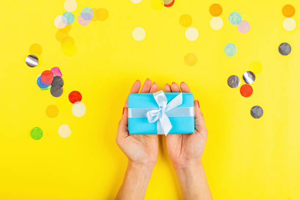 istock hand holding gift box on yellow background 1213985159