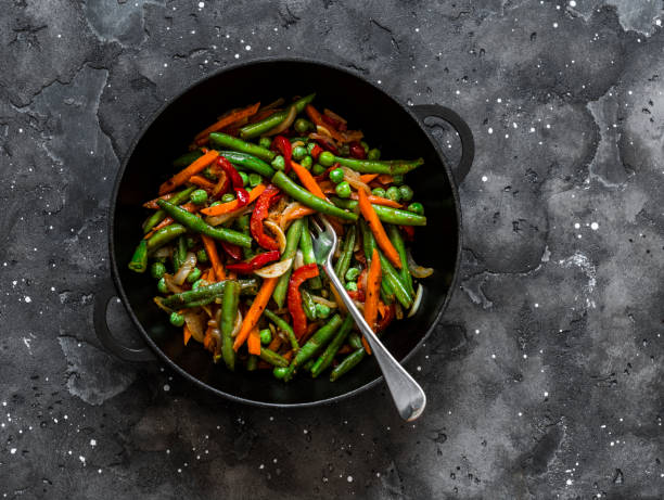 green beans, sweet peppers, carrots, onions, green peas stir fry in a pan on a dark background, top view. fast diet vegetarian lunch - bean vegetarian food stir fried carrot imagens e fotografias de stock