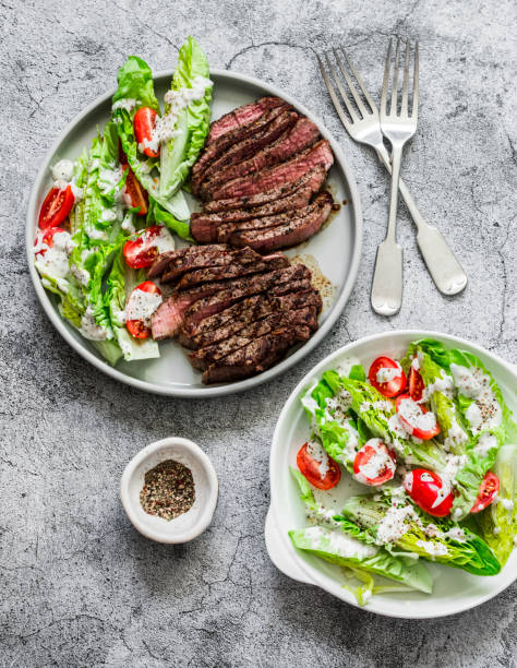 istock Beef medium rare steak and romaine salad cherry tomatoes yogurt dressing salad on a gray background, top view 1213988657