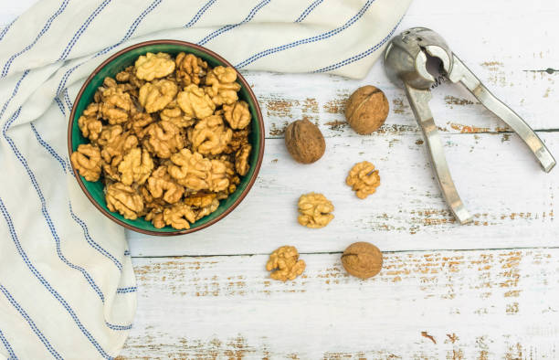 istock Peeled walnuts in a plate and nut cracker on a light wooden background. View from above. 1214005109