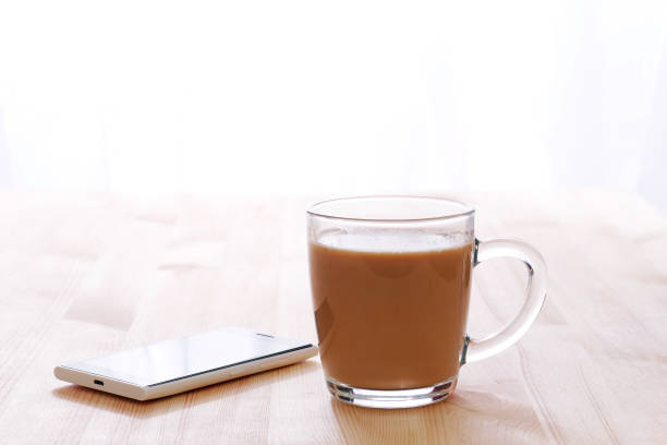 glass coffee with milk mug and smartphone lit by morning sunlight on a wooden table, copy space - wakening imagens e fotografias de stock