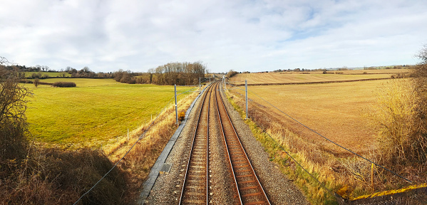 Electrified railway line in the English countryside. Rural line between fields shot in Panoramic format