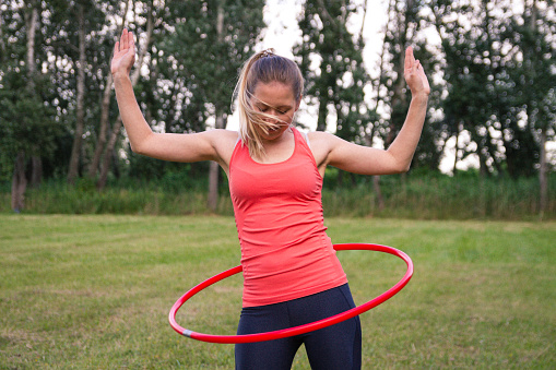 Fit woman is spinning plastic hoop in the park.