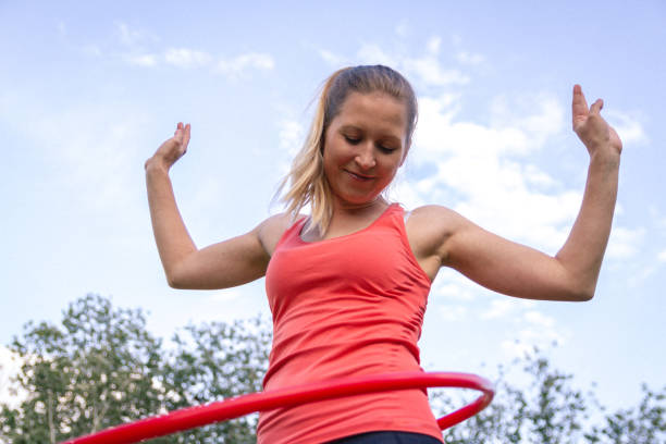 istock Joyful woman spinning plastic hoop against sky 1214018370