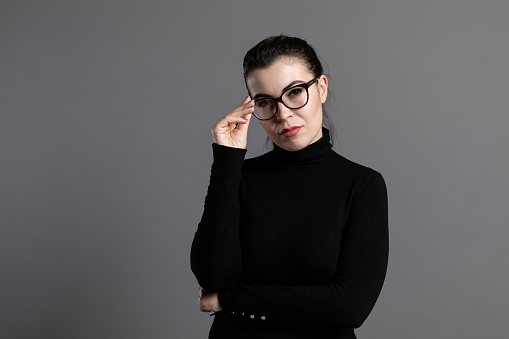 Portrait of young woman in black dress wearing glasses.