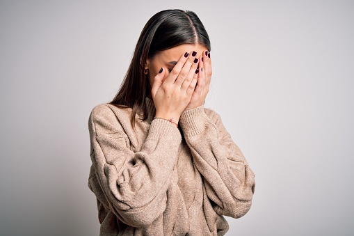 Young beautiful brunette woman wearing casual sweater standing over white background with sad expression covering face with hands while crying. Depression concept.