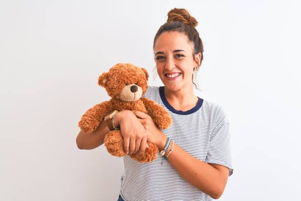 istock Young beautiful redhead woman holding stuffed teddy bear over isolated background with a happy face standing and smiling with a confident smile showing teeth 1214021349