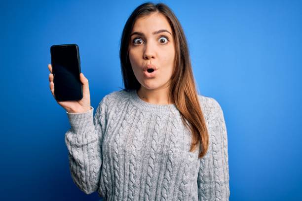 istock Young woman showing blank smartphone screen over blue isolated background scared in shock with a surprise face, afraid and excited with fear expression 1214023298