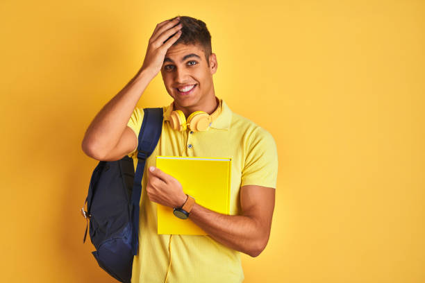 istock Indian student man wearing backpack headphones notebook over isolated yellow background stressed with hand on head, shocked with shame and surprise face, angry and frustrated. Fear and upset for mistake. 1214024618
