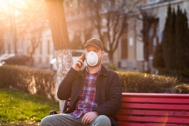 istock Man wearing protective face mask talking on phone in city park 1214028374