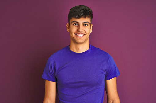 Young indian man wearing t-shirt standing over isolated purple background with a happy and cool smile on face. Lucky person.