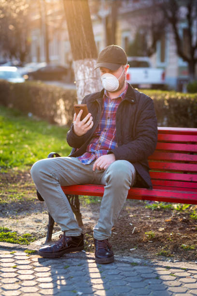 istock Man wearing protective face mask using smart phone in city park 1214030492